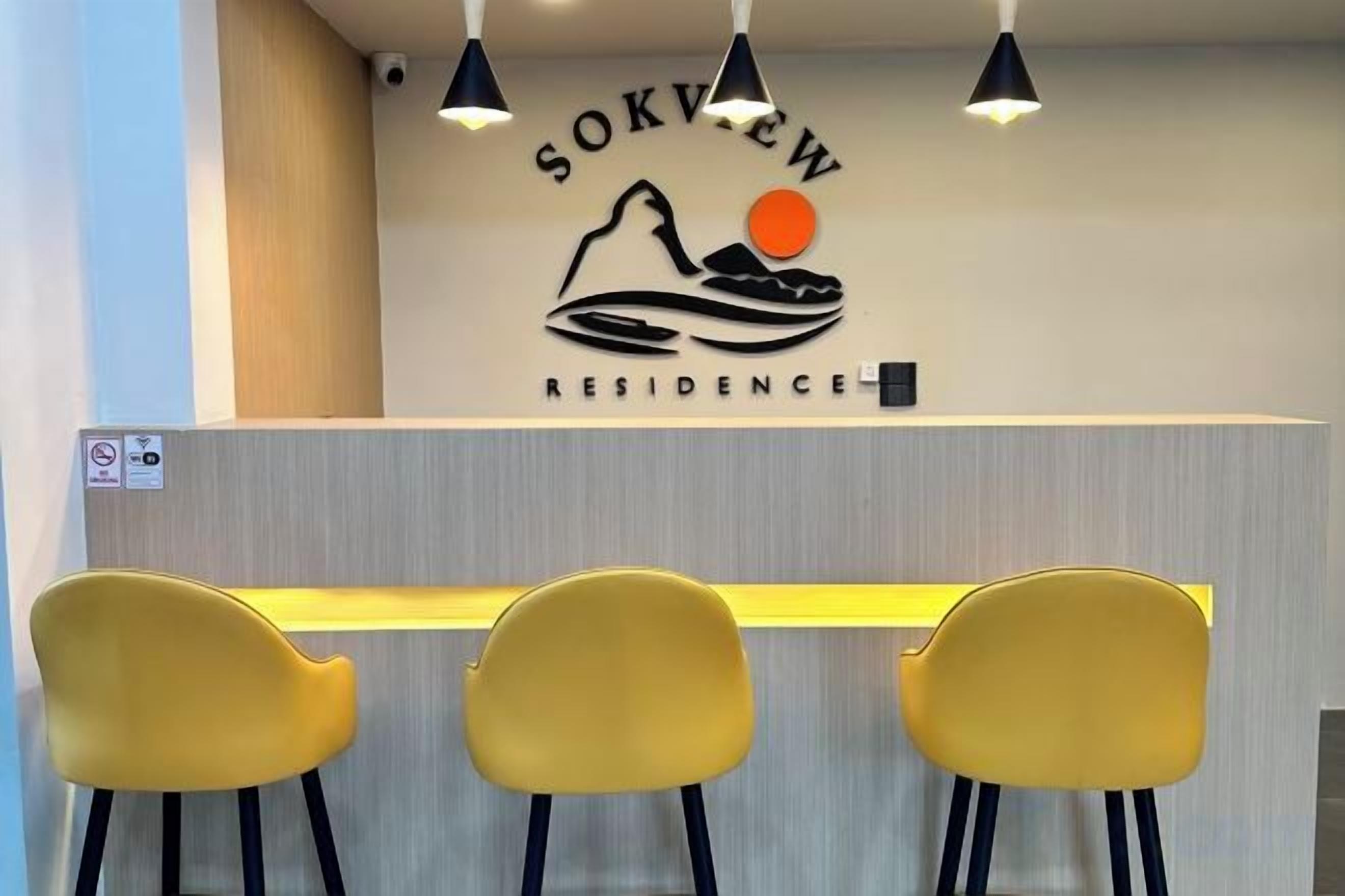 A reception area with a logo for Sokview Residence, three yellow chairs, and pendant lighting.