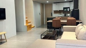 A modern living room with a sofa, coffee table, and a TV. There is a kitchen area with cabinets and a dining table. - Sokview Residence (Luang Prabang)