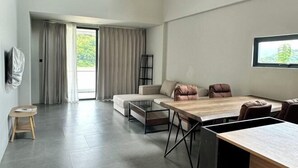 A modern living room with a sofa, a coffee table, a dining table with chairs, a TV mounted on the wall, and a window with curtains. - Sokview Residence (Luang Prabang)