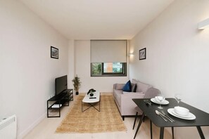 A modern living room with a sofa, a coffee table, a TV, and a dining table set for two. - Modern 1 Bed Apt Near Ascot- with parking (Bracknell)