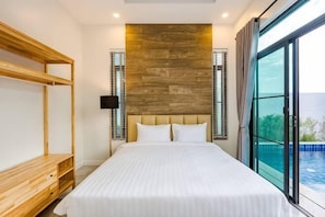 A bedroom with a bed, wooden headboard, a nightstand, a TV, and a view of the sea.