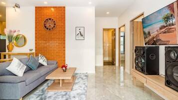 A modern living room with a gray sofa, a coffee table, a brick accent wall, a large TV, and a pair of speakers.