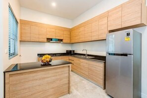 A modern kitchen with wooden cabinets, a stainless steel refrigerator, and a black countertop. - Me&You Pool Villa Hua Hin (Cha-am)
