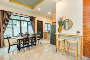 A dining area with a table set for four, a kitchen area with a refrigerator, and a mirror on the wall. - Me&You Pool Villa Hua Hin (Cha-am)