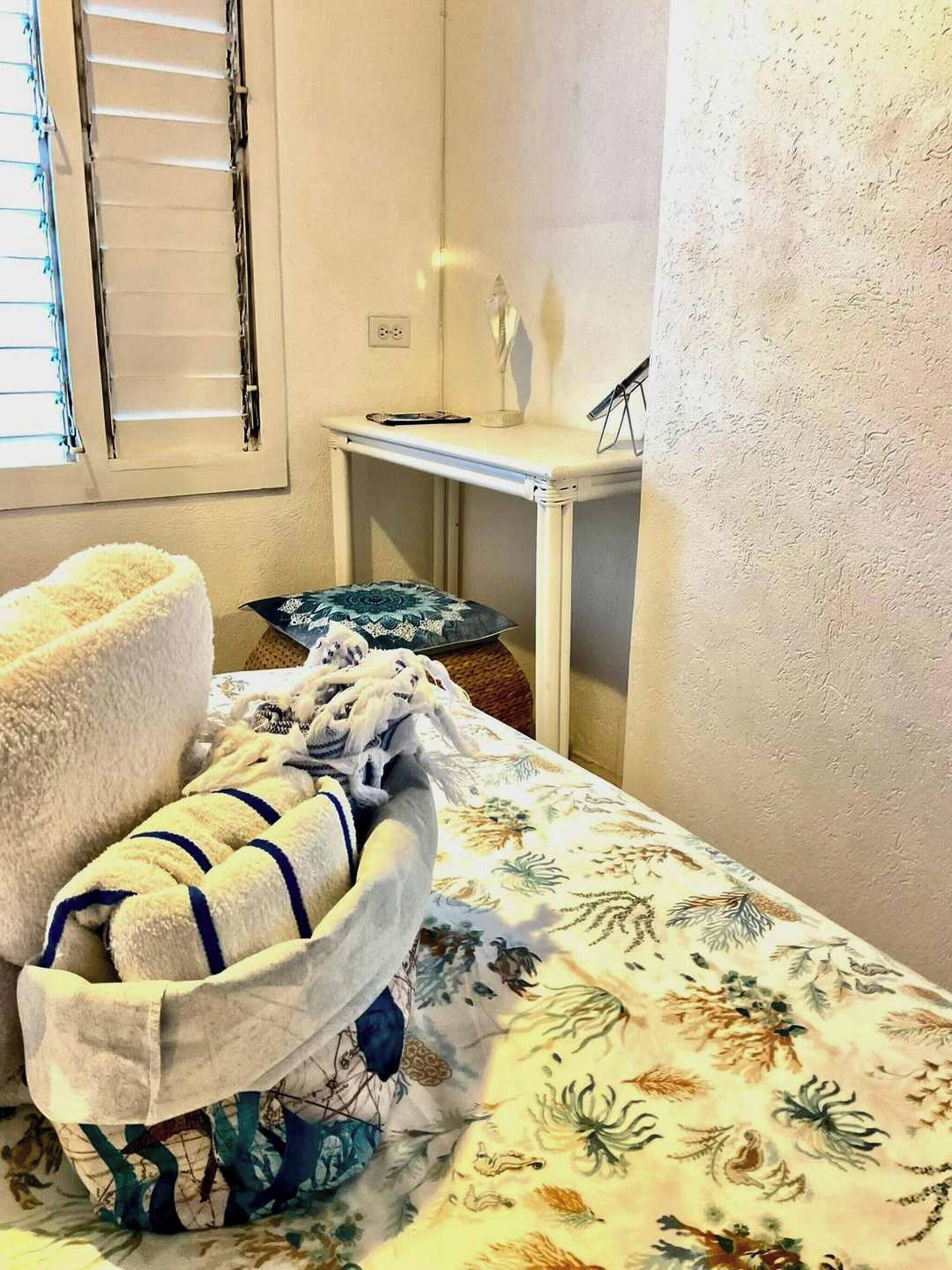 Une petite chambre à coucher, bien rangée, avec un lit, une table de chevet et une fenêtre équipée de stores.