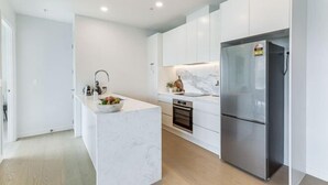 Een moderne keuken met witte kasten, een marmeren aanrechtblad, een roestvrijstalen koelkast en een inbouwoven.