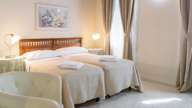 A hotel room with two beds, a bedside table with a lamp, a chair, and a painting on the wall. - Juliet House (Verona)