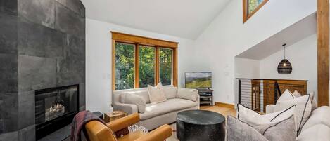 Una sala de estar moderna con chimenea, un conjunto de sofás, una silla de madera y un televisor.