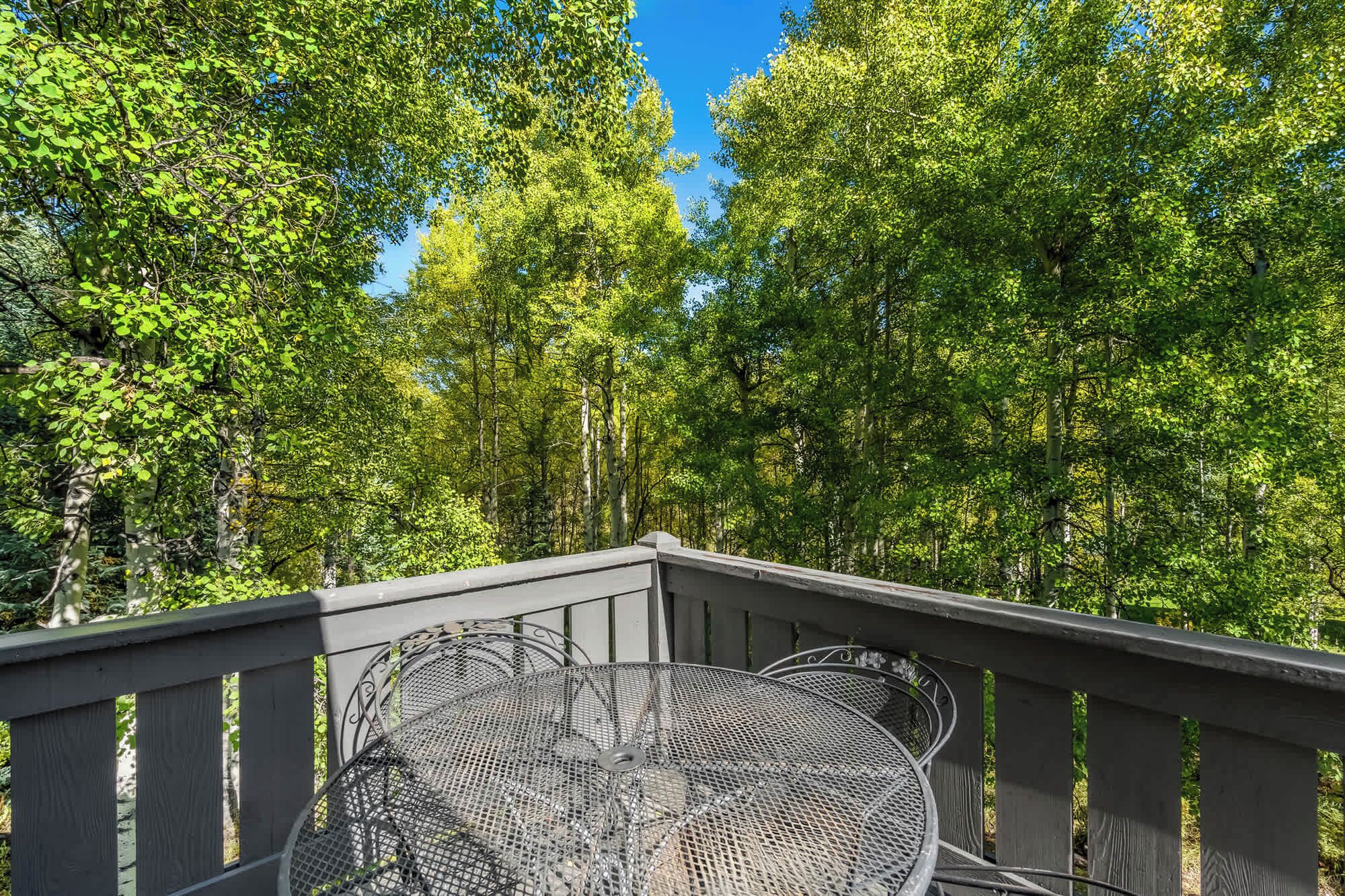 Ein Sitzbereich im Freien aus Metall mit Tisch und Stühlen, umgeben von einer Holzterrasse und üppigen Grünflächen.