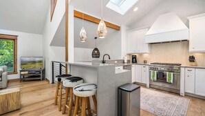 Una cucina moderna con isola centrale, sgabelli in legno, piano cottura integrato e un lucernario.