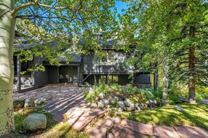 A rustic cabin with a stone pathway leading to the entrance, surrounded by lush greenery and trees.