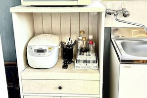 Una kitchenette con una cocedora de arroz, una botella de agua y una botella de aceite de oliva.