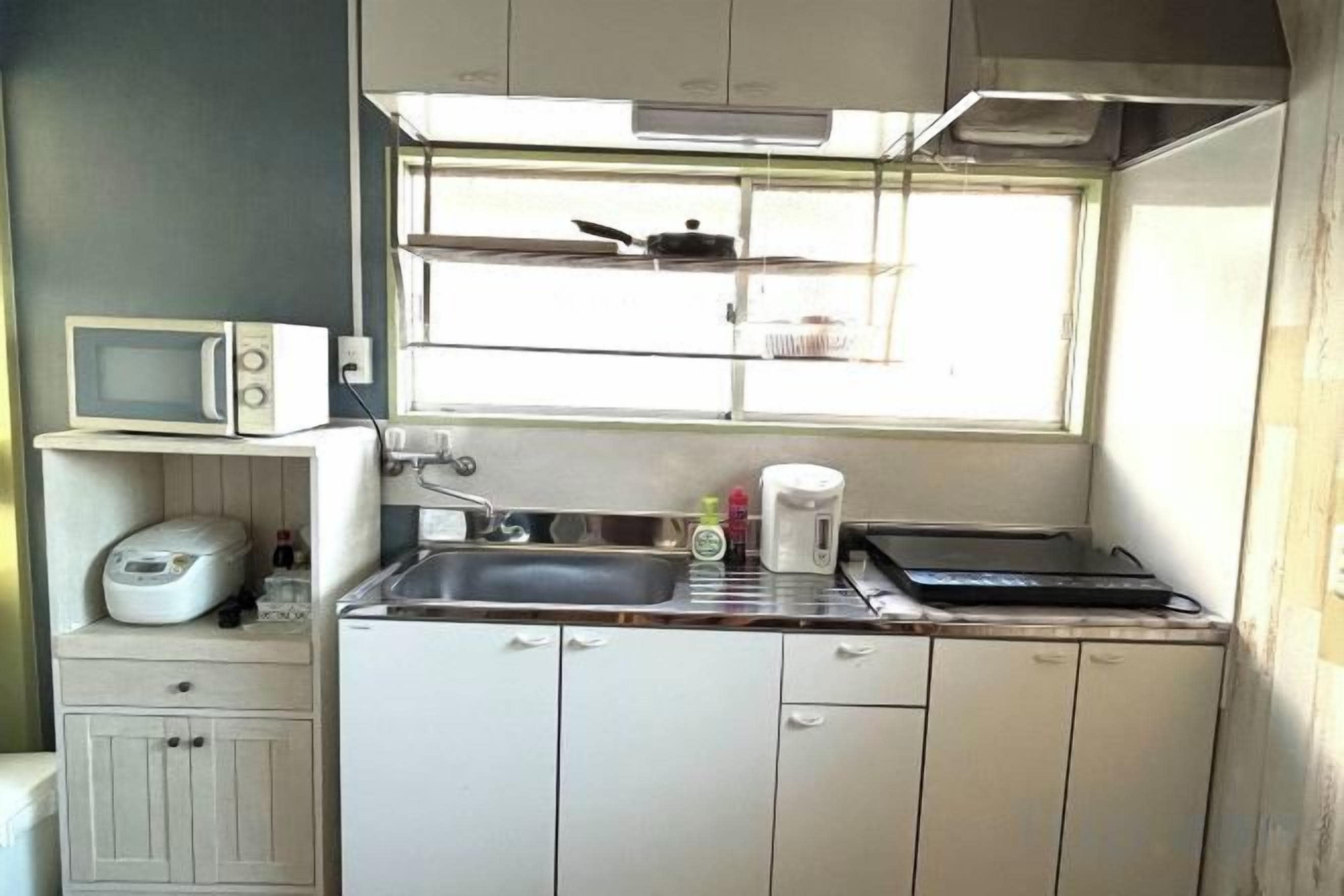 Uma cozinha compacta com micro-ondas, fogão, pia e janela sobre a bancada.