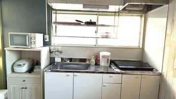 Uma cozinha compacta com micro-ondas, fogão, pia e janela sobre a bancada.