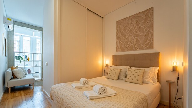 Une chambre à coucher avec un grand lit, deux tables de chevet, une œuvre d’art accrochée au mur et une fenêtre donnant sur l’extérieur.