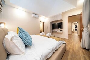 A modern bedroom with a bed, a flat-screen TV, and a wooden floor. - patong hill 3 villa (Phuket)