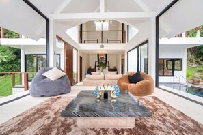 A modern interior with a large window, a sofa, a bean bag, and a coffee table. - patong hill 3 villa (Phuket)