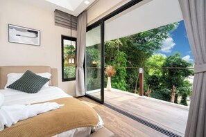 A bedroom with a large sliding glass door leading to a balcony with a view of trees and sky.