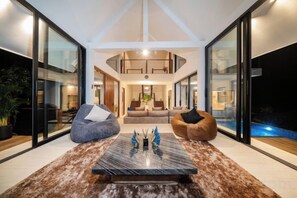 A modern interior with a central seating area, a pool visible through glass walls, and a high ceiling. - patong hill 3 villa (Phuket)