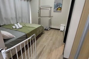 A bedroom with a bed, a nightstand, a radiator, a drying rack, and a painting on the wall. - Near MOA beside Okada Pet Friendly 1BR 3 pax WIFI 8T (Paranaque)