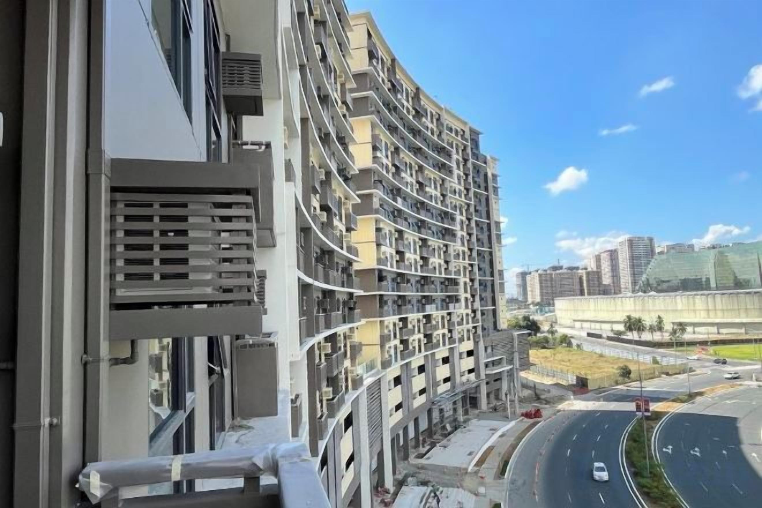 A high-rise building with multiple balconies and a view of a curved road with vehicles.