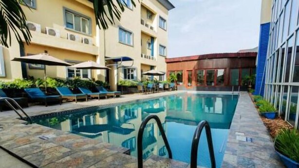 A swimming pool with lounge chairs and umbrellas, surrounded by a stone deck. - Sunfit International Limited (Lagos)