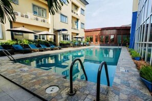 A swimming pool with lounge chairs and umbrellas, surrounded by a stone deck. - Sunfit International Limited (Lagos)