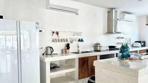 A modern kitchen with a white countertop, wooden cabinets, and a hanging utensil rack. - Metero Garden Swimming Pool Villa (Pattaya)