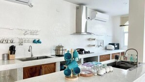 A modern kitchen with white walls, stainless steel appliances, and a central island with a mug rack. - Metero Garden Swimming Pool Villa (Pattaya)