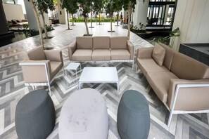 Un área de estar al aire libre moderna con suelo de diseño espiga, un sofá color beige, dos sillones y una mesita blanca.
