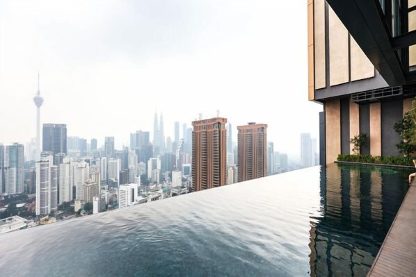 Un edificio moderno con piscina infinita en la azotea que ofrece vistas a un horizonte urbano.