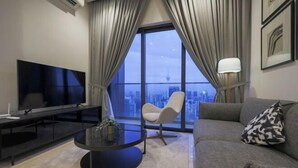 A modern living room with a large TV, a round coffee table, a sofa, and a chair. - Lucentia Residence at Kuala Lumpur by Dreamcloud Sdn Bhd (Kuala Lumpur)