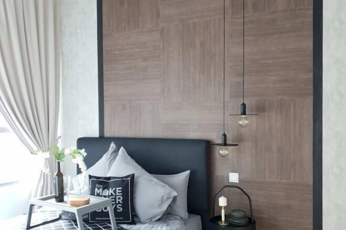 A modern bedroom with a bed, a bedside table with a vase and a book, a wall-mounted light fixture, and a decorative wall panel.