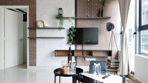 Un salon moderne doté d’un téléviseur à écran plat, d’étagères en bois, d’une table ronde ornée de bouteilles et d’un lampadaire suspendu.