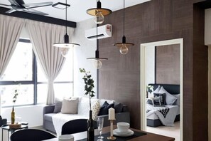 Moderni hotellihuone, jossa on suuri ikkuna, sohva, ruokapöytä ja kynttilä sekä kattotuuletin.