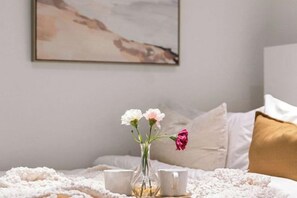 A bed with a white blanket, a vase with flowers, and two cups on a bedside table. - A Cozy CBD Studio Near Melbourne Central (Melbourne)