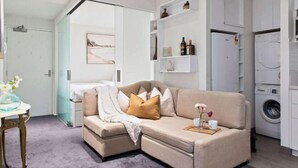 Un moderno salón con un sofá color beige, una mesa de centro con un jarrón y una lavadora al fondo.