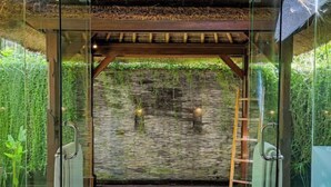A glass-enclosed room with a stone wall, a wooden ladder, and a thatched roof. - Villa Melissa (Bali)