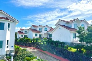 A row of white houses with red roofs, arranged in a row, with a stone wall and greenery in the foreground. - Tebaz (Jeju)