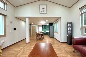 A spacious living area with a wooden floor, a dining table, and a red sofa. - Tebaz (Jeju)