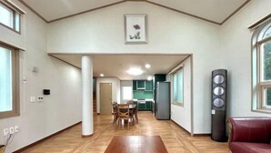 A spacious living room with a wooden floor, a dining area, and a kitchen visible through an open doorway. - Tebaz (Jeju)