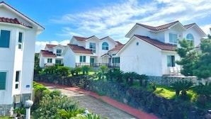 A row of white villas with red-tiled roofs, arranged in a row with a stone wall and greenery in the foreground. - Tebaz (Jeju)