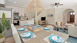 A modern living room with a dining area, kitchen, and a ceiling fan.