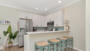 A modern kitchen with white cabinets, stainless steel appliances, and a bar area with stools.