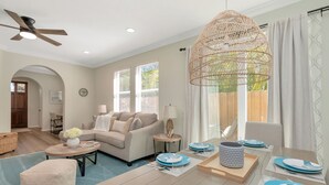 A modern living room with a sofa, coffee table, and dining area set with blue plates and a woven light fixture.