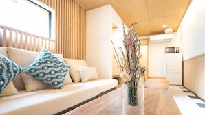 A wooden table with a vase of dried branches, a sofa with patterned cushions, and a wooden slatted wall.