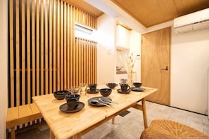 A dining table with black bowls and chopsticks, a woven chair, and a wooden partition. - INN Plus Hanamidou (Kyoto)