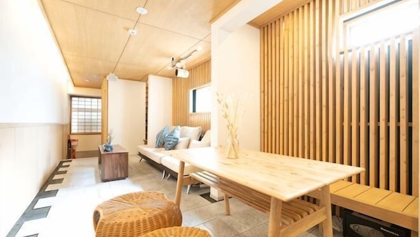 A modern interior with a wooden dining table, two wicker chairs, a sofa, and a wooden wall paneling.