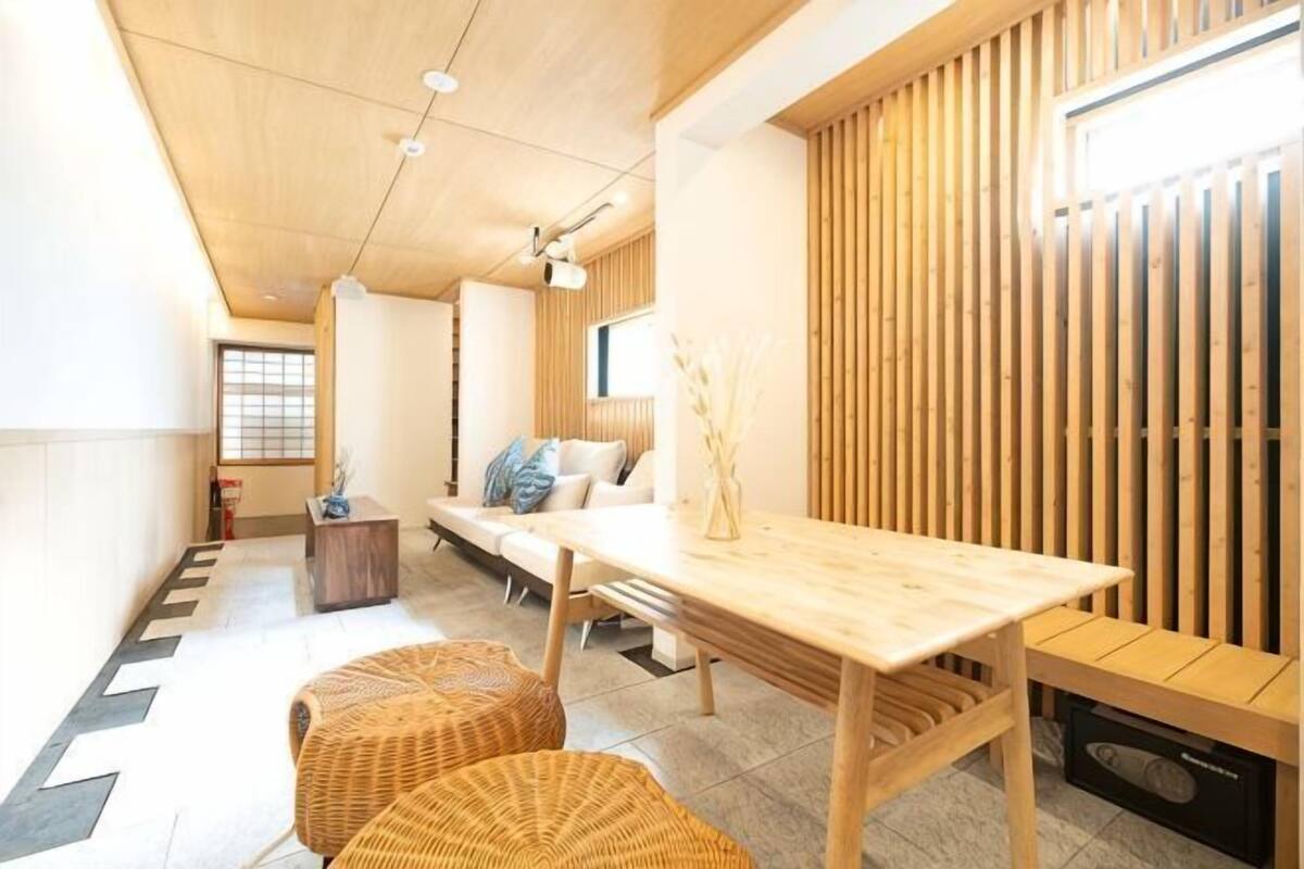 A modern interior with a wooden dining table, two wicker chairs, a sofa, and a wooden wall paneling.