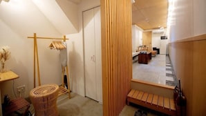 A hallway with a wooden floor, a small table with a vase, a wicker chair, and a wooden bench.